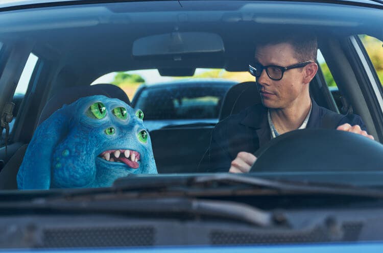 Creature and a man driving with one another in a car